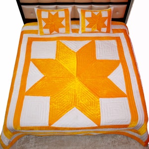 May include: A quilted bedspread and two matching pillow shams. The bedding features a large star design in bright yellow and white. The star is centered on the bedspread, with a white border and yellow accents. The pillow shams have a star design.