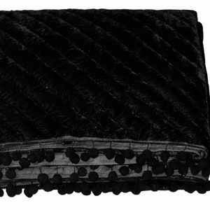 May include: A folded black blanket with a quilted, diagonal pattern. The blanket is trimmed with a row of black pom-poms along the edge. The blanket appears to be made of a soft, plush material.