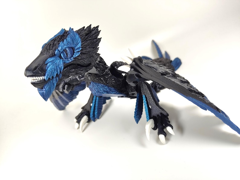 May include: A detailed figurine of a dragon with a black body and blue accents. The dragon has a feathered head, wings, and tail. Its claws and teeth are white. The figurine is posed on a white surface.