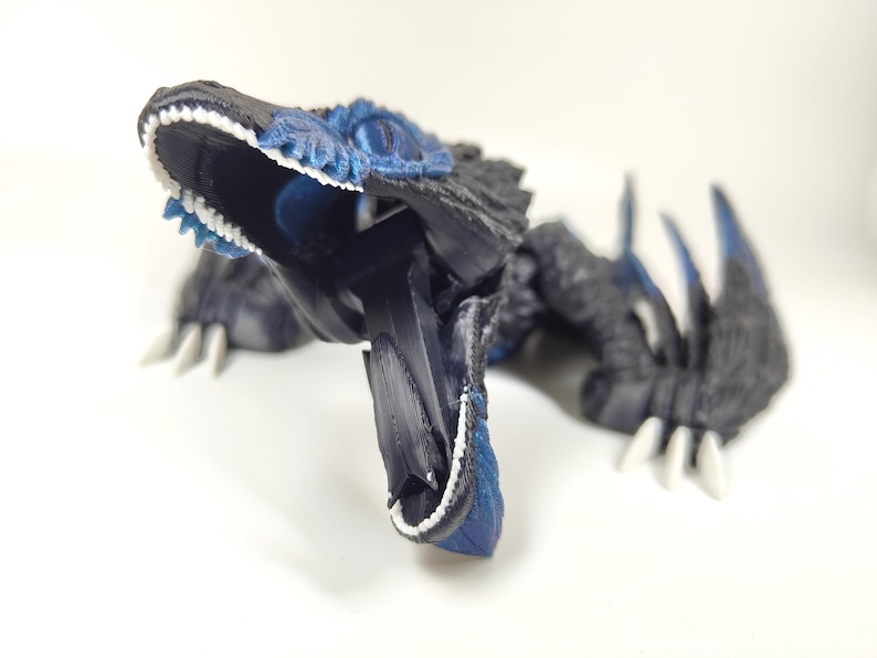 May include: A detailed, 3D-printed dinosaur figurine in shades of black and blue, with white teeth and claws. The open-mouthed creature has textured details and a dynamic pose, showcasing its sharp teeth and claws.