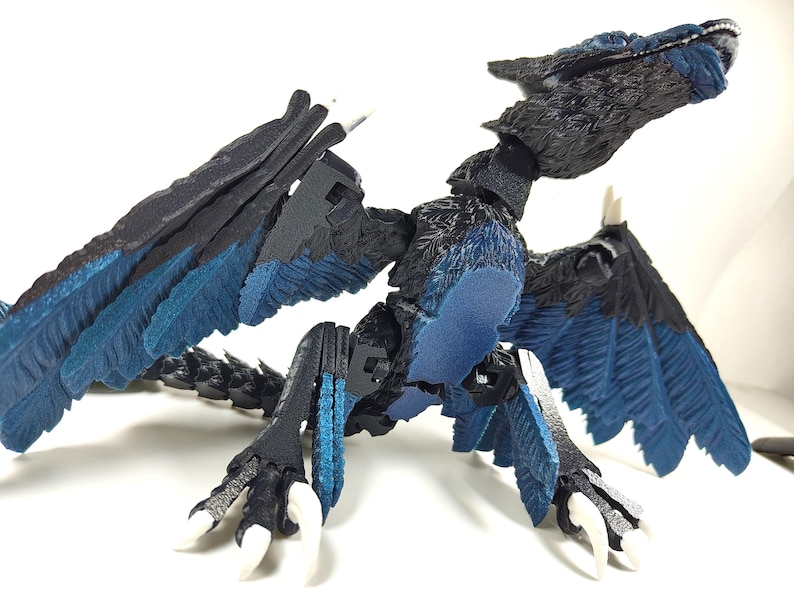 May include: A detailed, articulated dragon figurine with a black and blue color scheme. The dragon has large wings, sharp claws, and a detailed head. The wings and chest feature a vibrant blue color, contrasting with the black body.