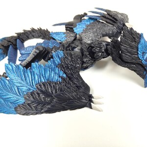 May include: A detailed, three-dimensional sculpture of a dragon with a combination of black, gray, and blue colors. The dragon has a detailed feather design on its wings and body, with white claws.