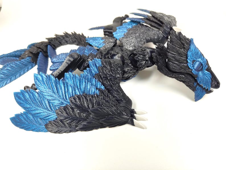 May include: A detailed, three-dimensional sculpture of a dragon with a combination of black, gray, and blue colors. The dragon has a detailed feather design on its wings and body, with white claws.