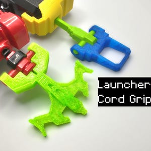 May include: Green, blue and red 3D printed launcher cord grips. The text "Launcher Cord Grips" is printed in black on a white background.