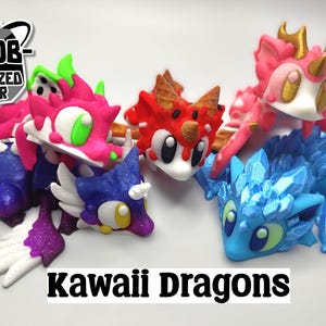 May include: Five 3D printed kawaii dragons in various colors, including pink, blue, red, and purple. The dragons have large eyes and are posed in a playful manner. The text "Kawaii Dragons" is printed below the dragons.