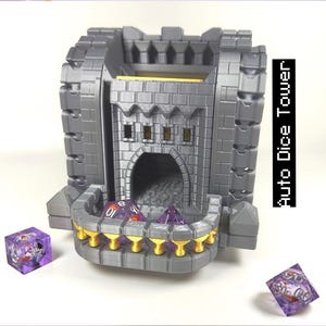 May include: A grey, castle-shaped dice tower with gold detailing and the text "Auto Dice Tower." Several purple dice are visible inside and around the tower. The tower has a detailed, textured design and a balcony.