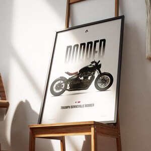 May include: Framed poster featuring a black Triumph Bonneville Bobber motorcycle. The word "BOBBED" is printed in large, stylized letters above the motorcycle. The text "TRIUMPH BONNEVILLE BOBBER" is printed below the motorcycle, with a small British flag icon.