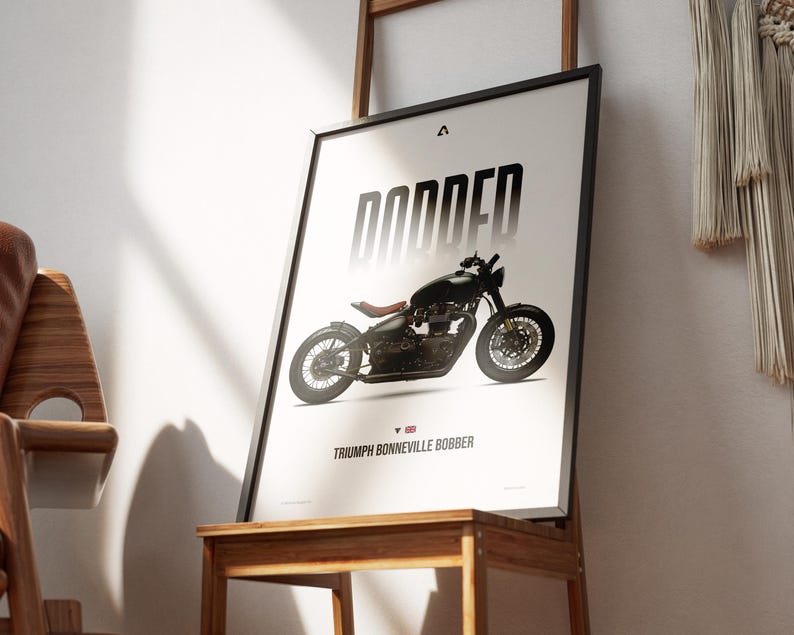 May include: Framed poster featuring a black Triumph Bonneville Bobber motorcycle. The word "BOBBED" is printed in large, stylized letters above the motorcycle. The text "TRIUMPH BONNEVILLE BOBBER" is printed below the motorcycle, with a small British flag icon.