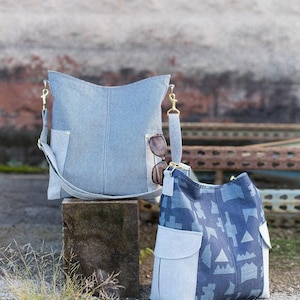 May include: Two hobo-style shoulder bags featuring light blue and dark blue fabric panels. The taller bag has a fine pinstripe pattern and gold-tone metal clips, while the shorter bag displays a geometric pattern with light blue side pockets.