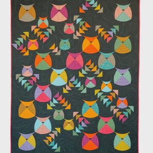May include: A rectangular quilt featuring a dark charcoal background with a subtle leaf pattern. The quilt is decorated with numerous stylised owl shapes and small triangle motifs in various bright colours including orange, pink, yellow, and teal.