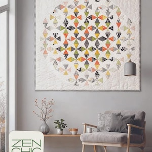 May include: A square quilt featuring a central circular pattern of diamond-shaped fabric pieces in orange, yellow, green, black, and white, set against a white background with intricate stitching. The text ZEN CHIC BRIGITTE HEITLAND DISSOLVE is visible.