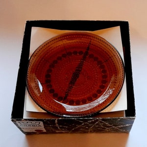 May include: A brown glass plate with a decorative pattern of small circles and dots. The plate is in a black box with the word "ARABIA" printed on the bottom.