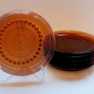 May include: A set of six amber-colored glass plates with a textured, dotted surface. The plates are stacked on top of each other.