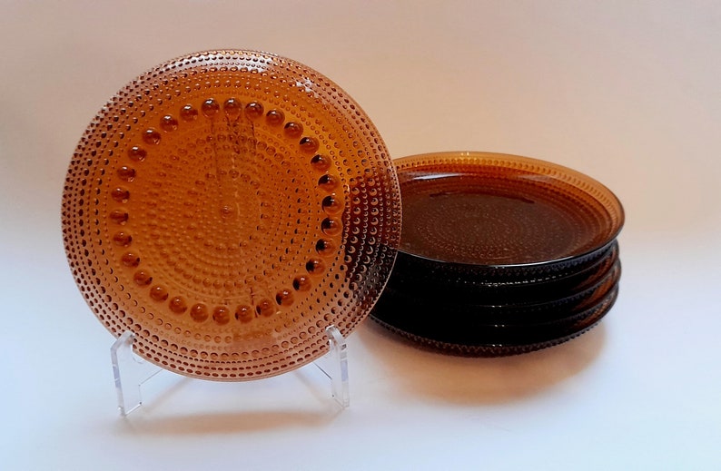 May include: A set of six amber-colored glass plates with a textured, dotted surface. The plates are stacked on top of each other.