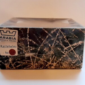 May include: A box with a black and white pattern of branches and a white frost design. The box has a label that says "Arabia W&auml;rtsil&auml; Finland" and "Kastehelmi No."
