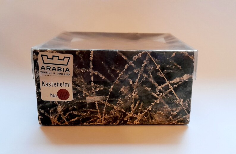 May include: A box with a black and white pattern of branches and a white frost design. The box has a label that says "Arabia W&auml;rtsil&auml; Finland" and "Kastehelmi No."