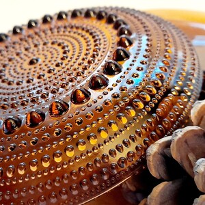 May include: A set of amber glass plates with a textured, dotted surface. The plates are stacked on top of each other and a pine cone is in the foreground.