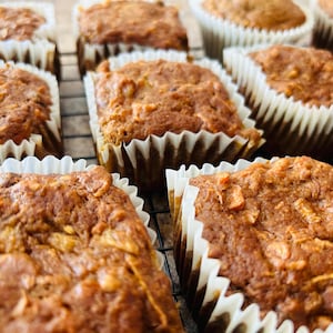 May include: Close-up of a batch of freshly baked muffins in white paper liners. The muffins have a light brown color and a slightly crumbly texture.