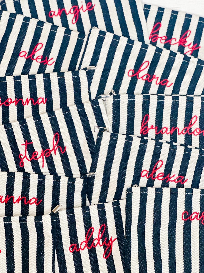 May include: Close-up of several navy and white striped pouches with names embroidered in pink thread. Names include Angie, Alex, Becky, Clara, Brandon, Alexa, Steph, Anna, Addy, and Cara.