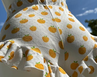 May include: White shorts with a pattern of yellow oranges and green leaves. The shorts have a ruffled hem. The shorts are displayed on a mannequin against a blue sky background.