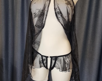 May include: Black lingerie set featuring a sheer, lacy top with spaghetti straps and a flowing, open front design. The set includes matching low-rise underwear with a delicate lace trim. The lingerie is displayed on a mannequin.