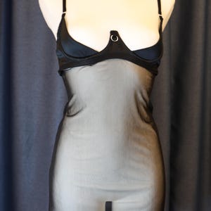 Peut inclure: Lingerie noire avec une jupe en tulle transparente et un corsage en satin avec un détail en anneau argenté. La lingerie est dotée d'un collier noir avec des fermoirs argentés.