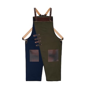 Könnte beinhalten: Zweifarbiges Latzschürze mit einzigartigem Design. Die Schürze hat ein marineblaues und olivgrünes Farbschema mit braunen Lederakzenten auf den Taschen, Trägern und dekorativen Details. Die Schürze hat zwei Vordertaschen und verstellbare Träger.