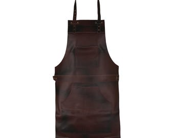 May include: A dark brown leather apron with a neck strap and waist strap. The apron has two large pockets and a loop for hanging. The leather has a distressed look.