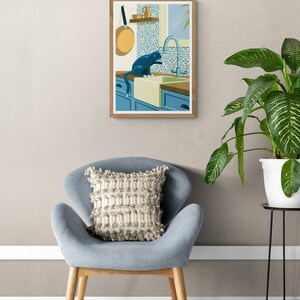Living room with a poster on the wall. The illustration on the art print shows a black cat in a kitchen with azulejo tiles as can often be found in Spain and Portugal. The artwork gives a Mediterranean feel. The cat is playing with dripping water.