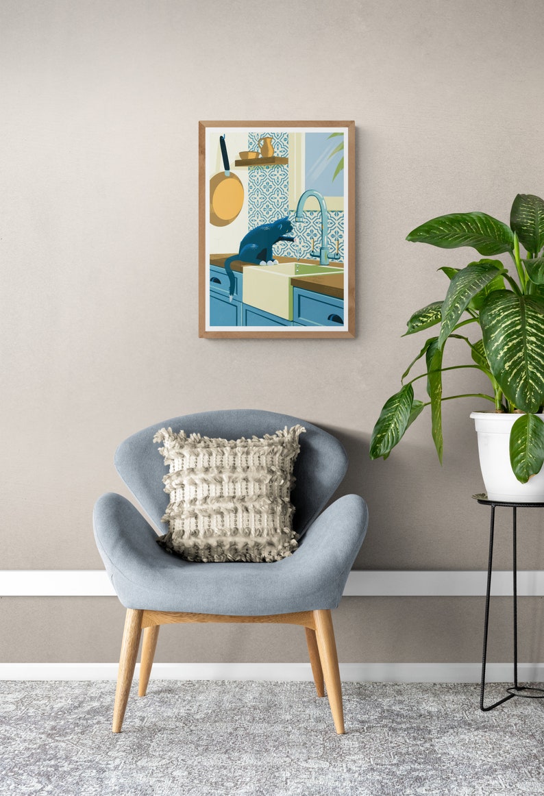 Living room with a poster on the wall. The illustration on the art print shows a black cat in a kitchen with azulejo tiles as can often be found in Spain and Portugal. The artwork gives a Mediterranean feel. The cat is playing with dripping water.