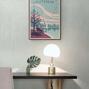 Home office with a poster or art print of an illustration of the city of Rotterdam in the Netherlands. It is a romantic scene of a couple sitting on a bench overlooking the river. Leaves drawn as hearts are flying through the sky.