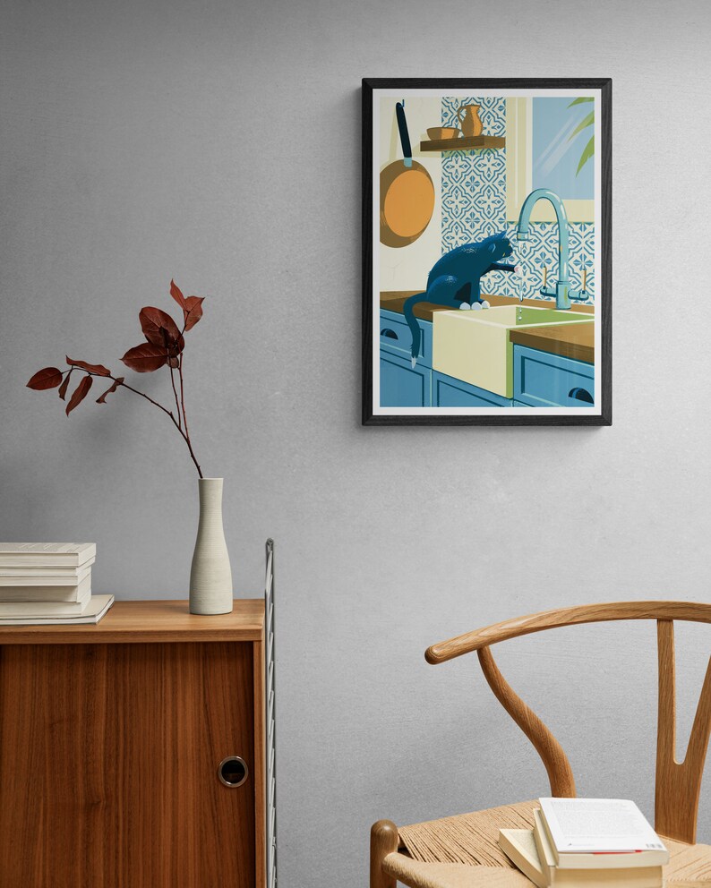 Living room with a poster on the wall. The illustration on the art print shows a black cat in a kitchen with azulejo tiles as can often be found in Spain and Portugal. The artwork gives a Mediterranean feel. The cat is playing with dripping water.