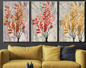 Puede incluir: Tríptico de impresiones artísticas abstractas de árboles. Cada lienzo presenta un árbol con hojas coloridas en tonos naranja, rojo y dorado sobre un fondo gris texturizado. La obra de arte se exhibe sobre un sofá amarillo en un salón moderno.