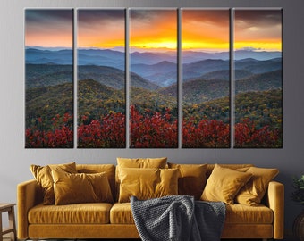 May include: A panoramic view of a mountain range with a vibrant sunset over the peaks. The foreground features a lush forest with red foliage in the fall season.