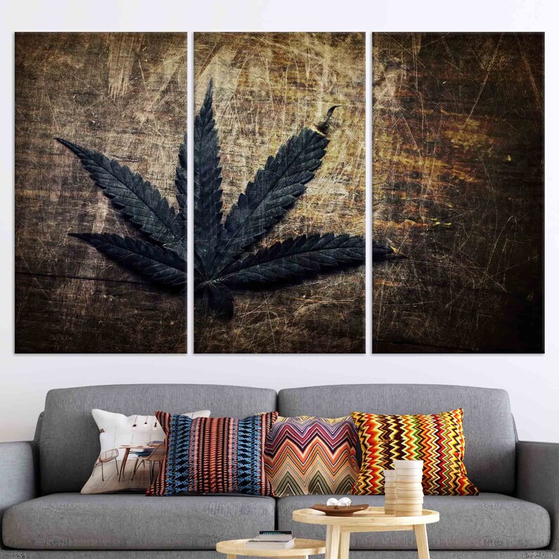 Puede incluir: Una impresi&oacute;n en lienzo de tres paneles con una hoja de marihuana verde oscuro sobre un fondo de madera desgastado.