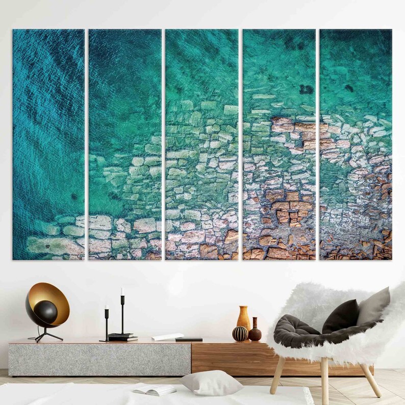 Op de afbeelding: Een meerdelige abstracte kunstprint met een turquoise en witte kleurstelling. De print toont een close-up van een rotsachtige kustlijn met turquoise water.