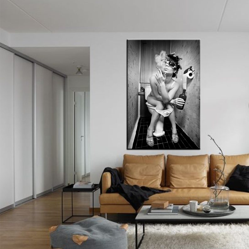 May include: Black and white wall art print of a person sitting on a toilet, smoking a cigarette, and holding a bottle. The person is wearing sunglasses and heels. The background is a bathroom.
