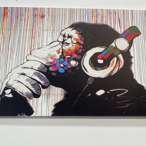May include: A black and white painting of a monkey wearing headphones. The monkey's face is covered in colourful paint splatters. The background is a white canvas with colourful vertical lines.