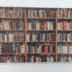 Puede incluir: Una estantería de madera llena de filas de libros coloridos. La estantería tiene tres estantes a cada lado y está hecha de madera oscura con un borde de madera clara. Los libros están dispuestos en una variedad de colores y tamaños.