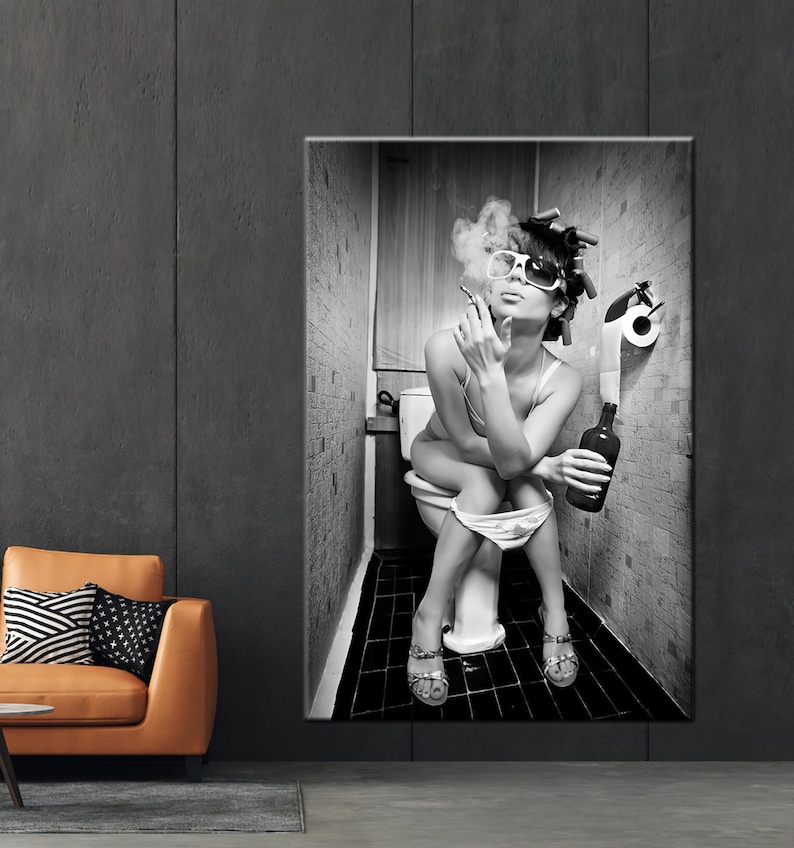 May include: Black and white wall art print of a person sitting on a toilet, smoking a cigarette, and holding a bottle. The person is wearing sunglasses and hair rollers. The bathroom has a roll of toilet paper.