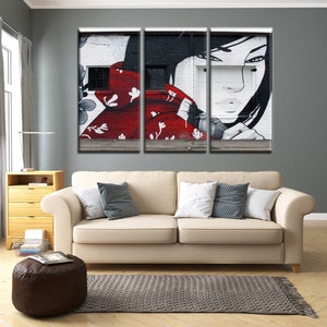 May include: A three-panel canvas print featuring a black and white graffiti mural of a woman with long black hair. The woman is wearing a red and white patterned scarf. The background is a white brick wall.