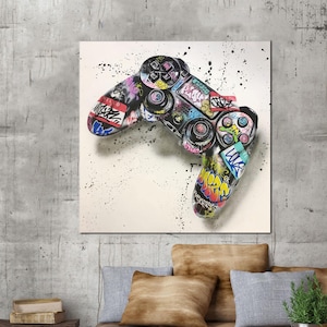May include: A colorful graffiti-style artwork of a video game controller. The controller is black with vibrant graffiti art in various colors, including pink, yellow, blue, and green. The background is white with black paint splatters.