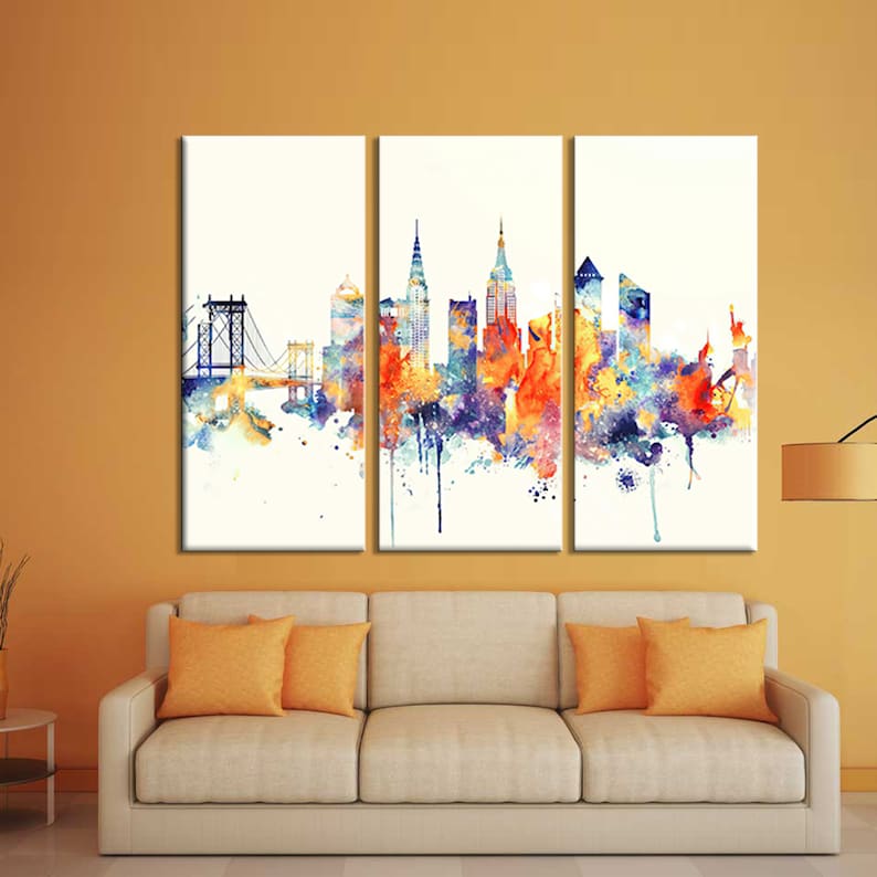 K&ouml;nnte beinhalten: Ein dreiteiliges Leinwandkunstwerk mit einer Aquarelldarstellung einer Stadtlandschaft. Das Kunstwerk zeigt eine lebendige Mischung aus Farben, darunter Orange, Blau und Lila, mit einer Br&uuml;cke und ikonischen Geb&auml;uden. Die Kunst wird &uuml;ber einem beigen Sofa mit orangefarbenen Kissen ausgestellt.