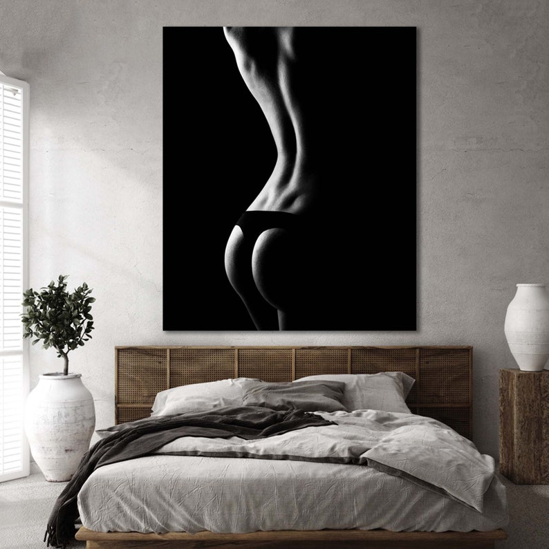 May include: Black and white photograph of a person's back in black underwear. The image is lit from the side, creating a dramatic silhouette.