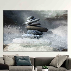 Puede incluir: Una pila de piedras grises y blancas equilibradas una encima de la otra, creando un jardín zen de piedras. Las piedras están rodeadas de agua blanca y un cielo gris y nublado.