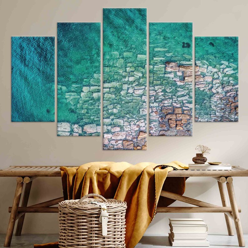 Op de afbeelding: Een vijfdelige canvas wandkunstset met een abstract luchtbeeld van een rotsachtige kustlijn met turquoise water. De afbeelding is verdeeld in vijf secties, die elk een ander deel van de sc&egrave;ne laten zien.