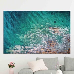 Op de afbeelding: Een luchtfoto van een rotsachtige kustlijn met turquoise water. De rotsen zijn een mix van wit, bruin en grijs, wat een getextureerd patroon cre&euml;ert.