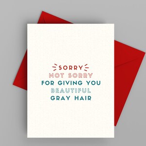 May include: A white card with red and blue text that reads "Sorry not sorry for giving you beautiful gray hair". The card is sitting on a red envelope.
