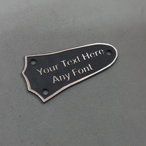 Puede incluir: P&uacute;a de guitarra negra con borde plateado. La p&uacute;a tiene el texto "Your Text Here Any Font" grabado.