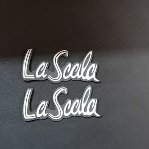 May include: Two silver-colored La Scala logos on a black background.